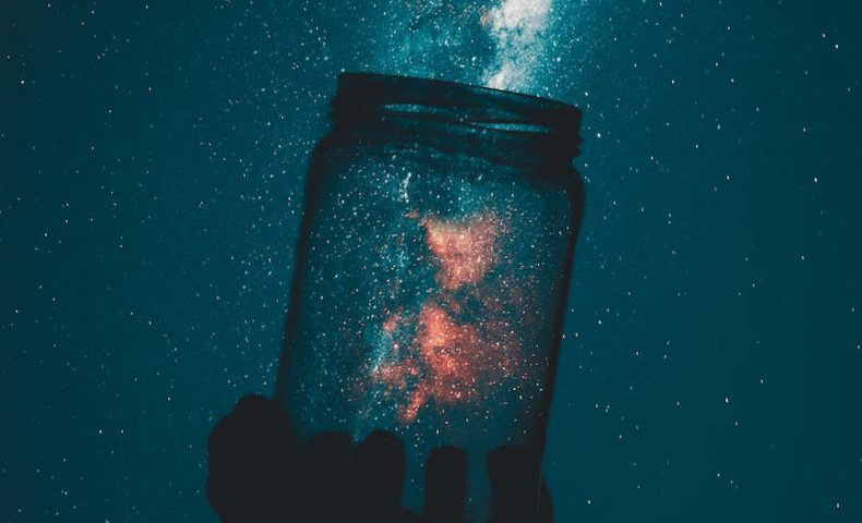 creative photo of person holding glass mason jar under a starry sky