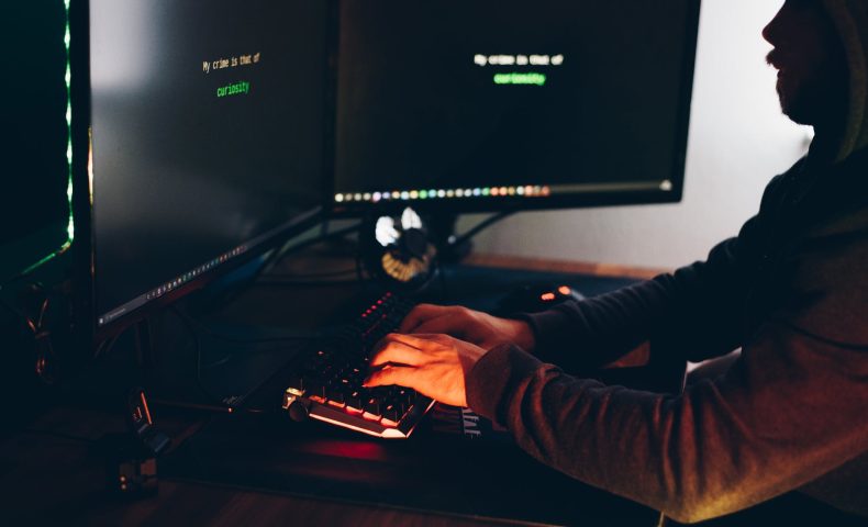 crop hacker silhouette typing on computer keyboard while hacking system