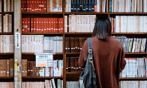woman wearing brown shirt carrying black leather bag on front of library books