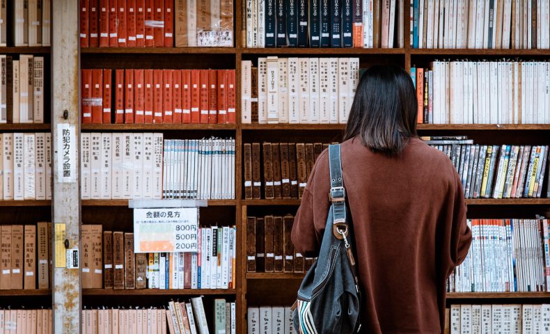 woman wearing brown shirt carrying black leather bag on front of library books