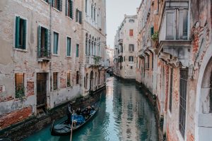 people riding boat on canal between concrete buildings